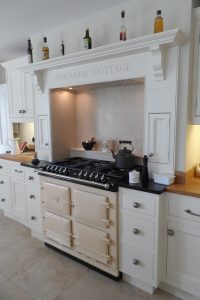 Family kitchen cabinets with personalised engraving above an Aga cooker and lit splash-back